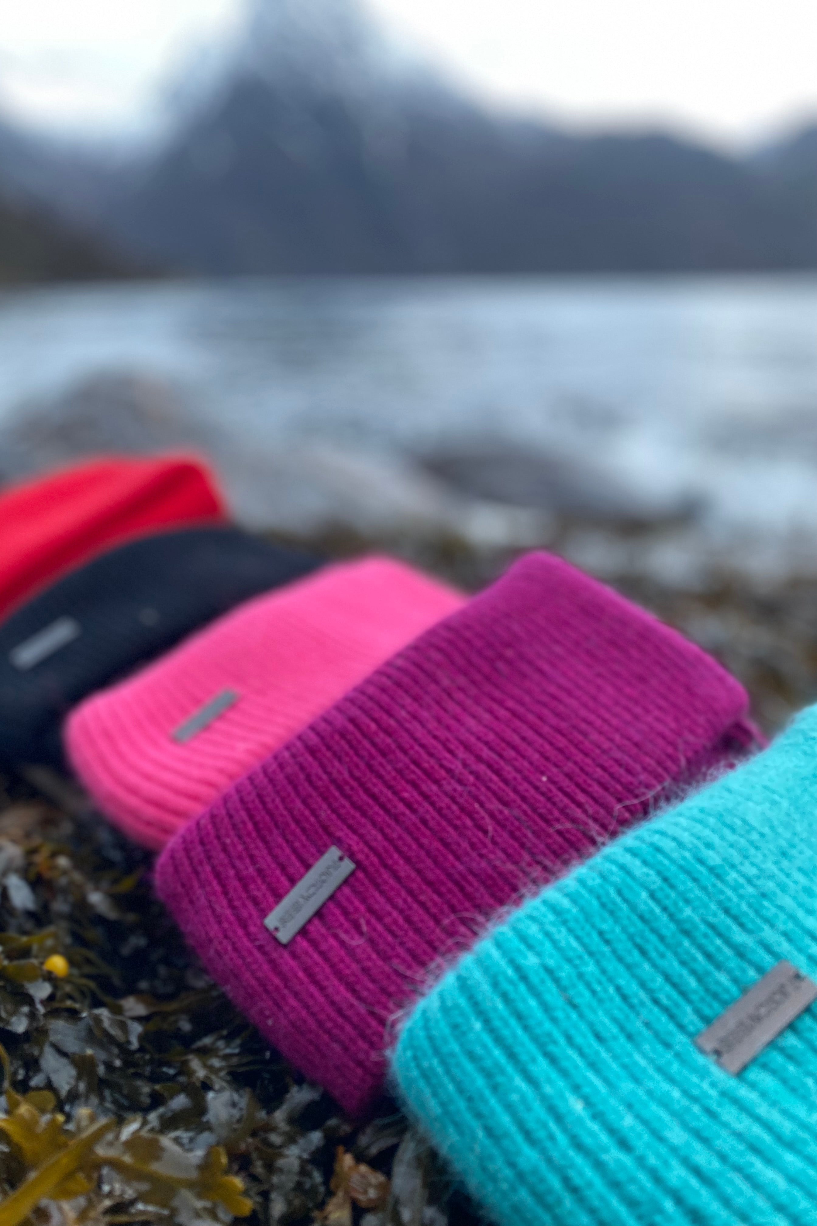 Fjord Vibes ull-luer ligger på rekke nede ved fjorden, i mange spreke farger